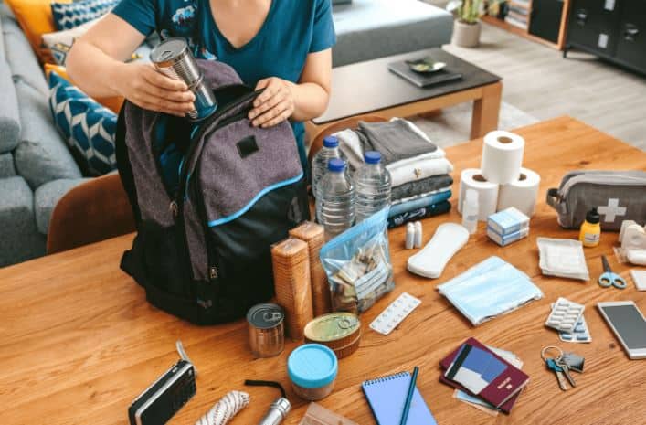 A bug out bag with plenty of items next to it on a wooden table.