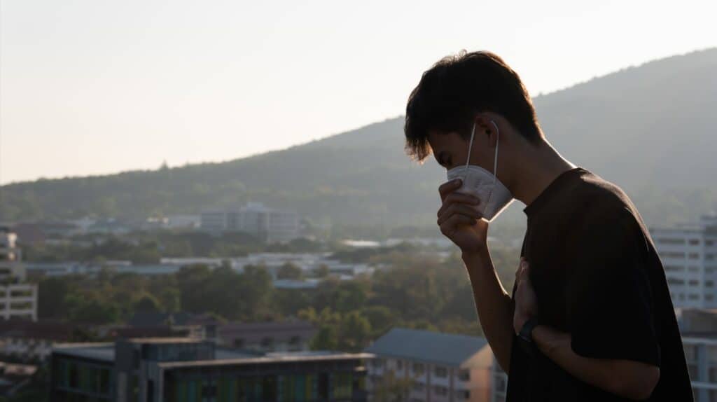 Picture of an asian man with an N95 mask in a dusty city background.